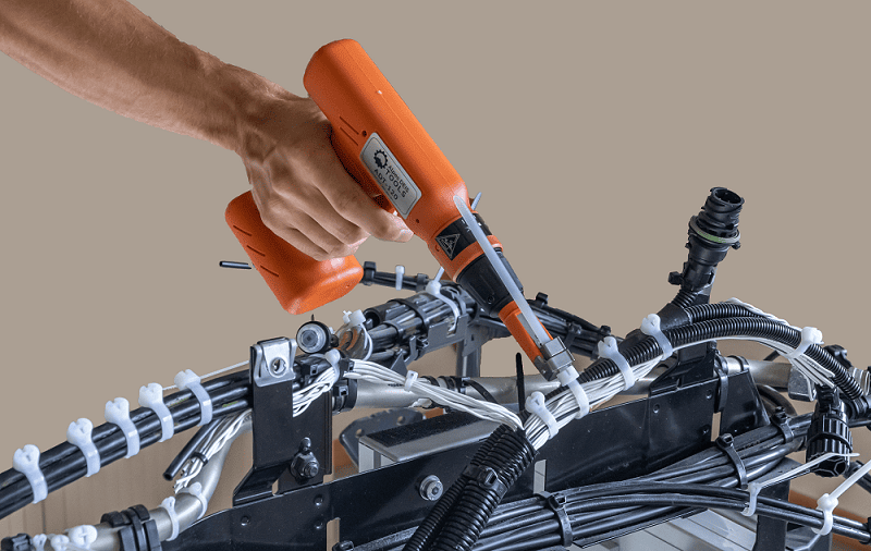 Tightening plastic cable ties on a bench representing a heavy vehicle chassis, using the ADT Tools ADT-120 battery-operated tool.